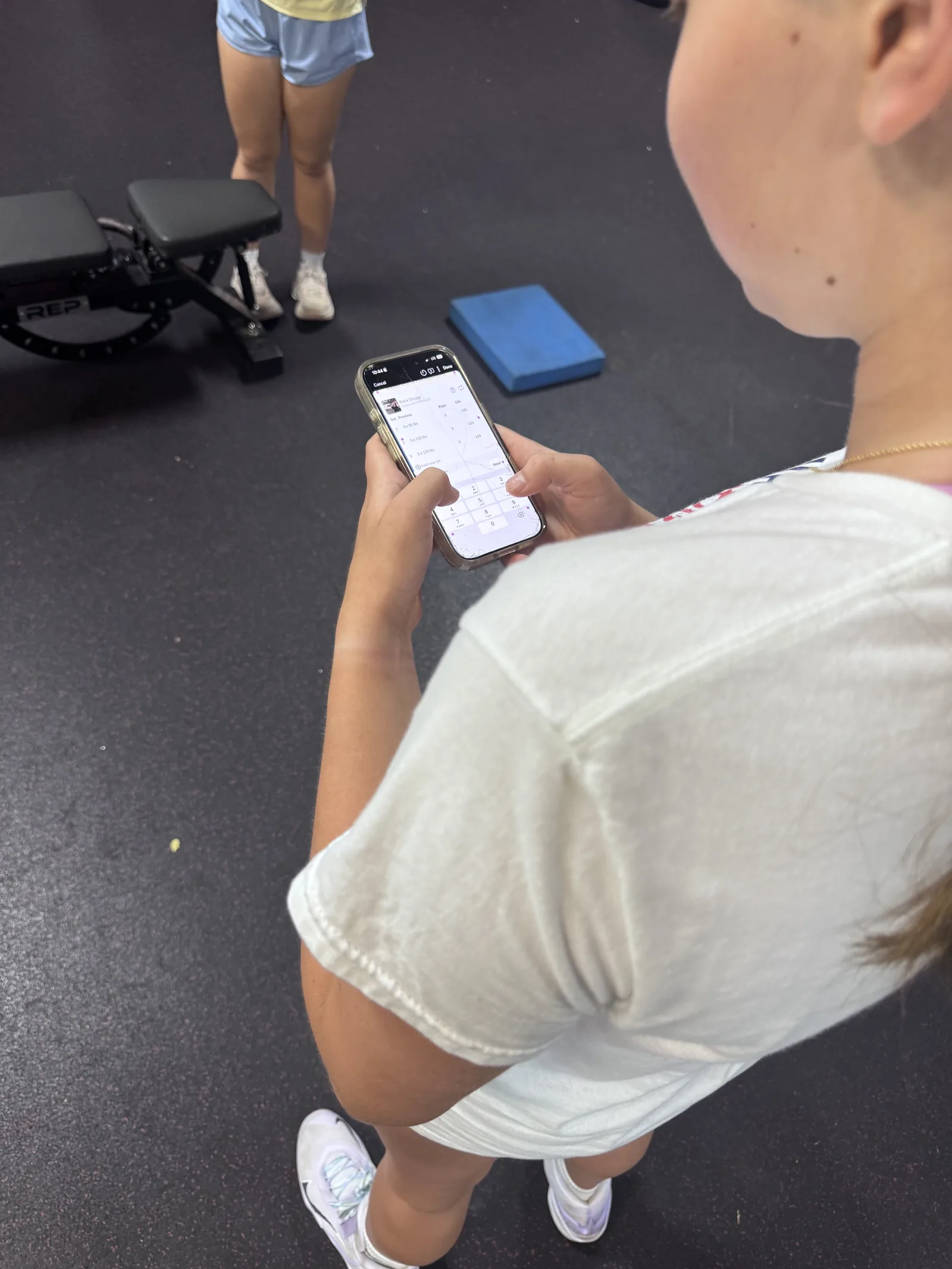 An athlete entering her numbers on her phone between sets