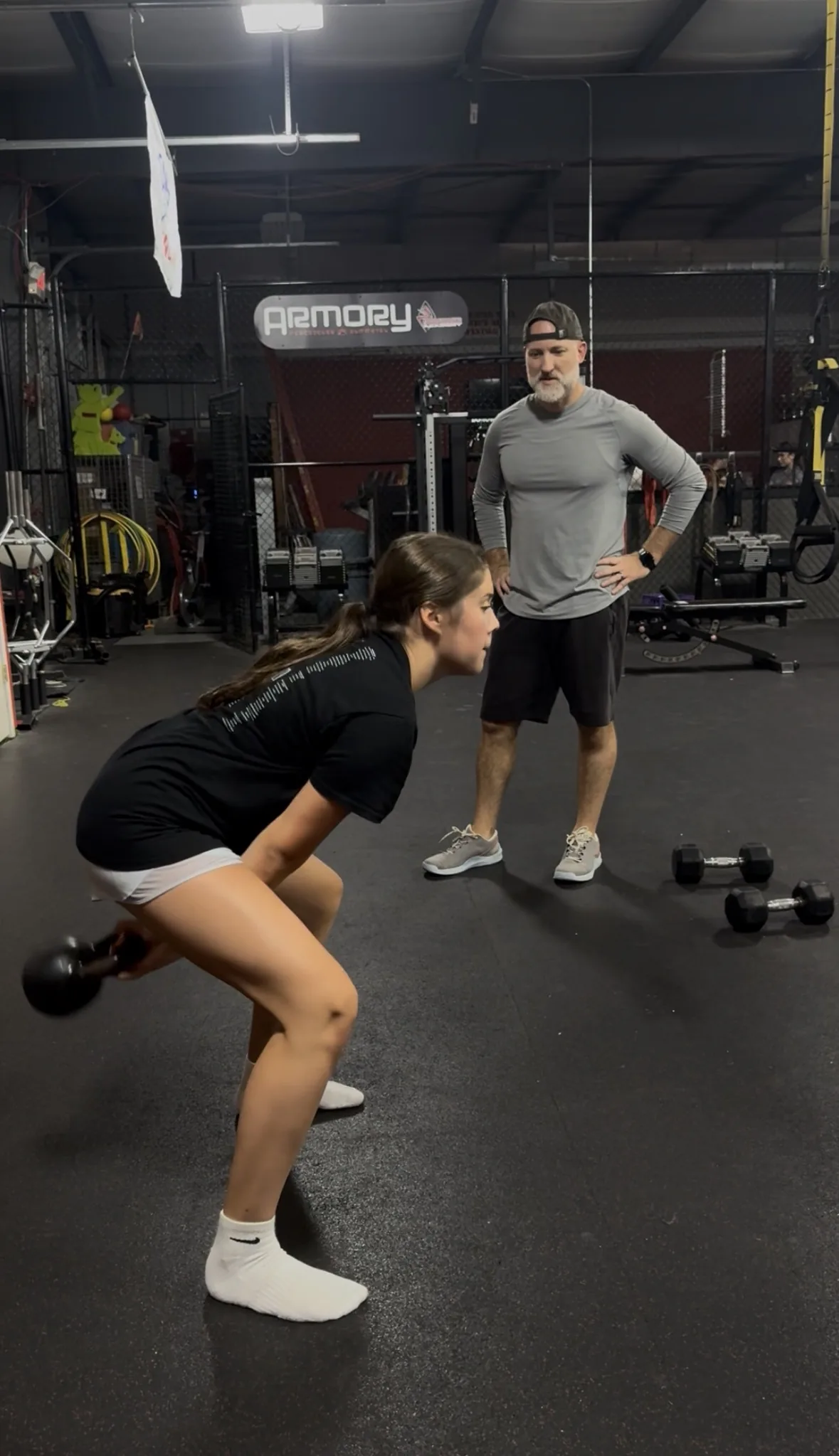 An athlete hinging back with a kettlebell while Coach Aaron watches her hip position